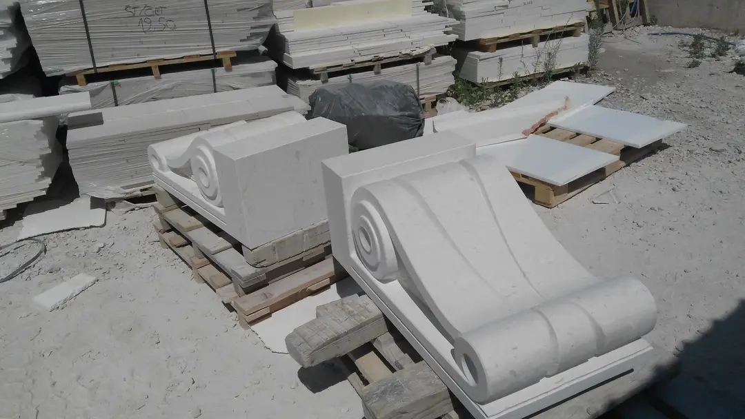 Dvije klesane volute od kamena Plano na paletama u krugu pogona, iza njih složene piljene ploče